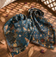 Midnight blue bird and floral silk scarf draped on a wooden surface.