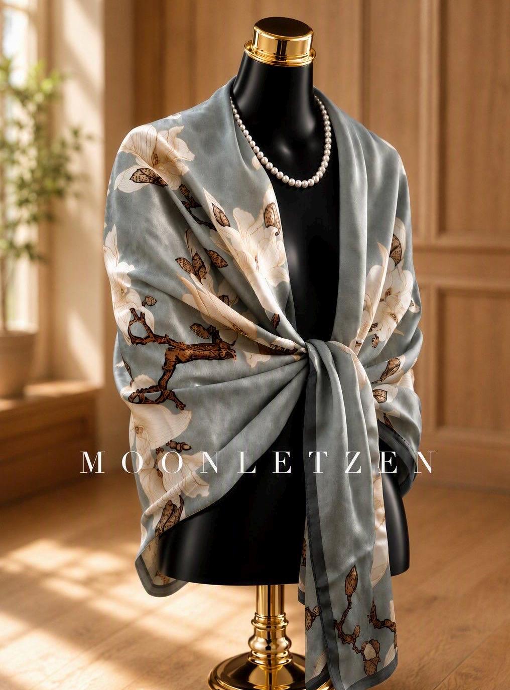Sage-grey silk wrap with white magnolia blossoms, tied across a mannequin's shoulders.
