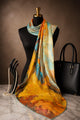 Amber and blue autumn-landscape silk scarf draped around a black mannequin.