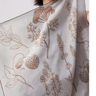 Close-up of brown botanical linework on a pale silk scarf.