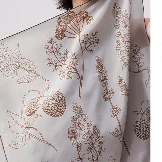 Close-up of brown botanical linework on a pale silk scarf.