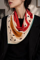 Ivory, coral-red and ochre silk scarf with a teal edge worn over black clothing.