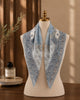 Light-blue and ivory paisley silk scarf draped on a mannequin with pointed folds.