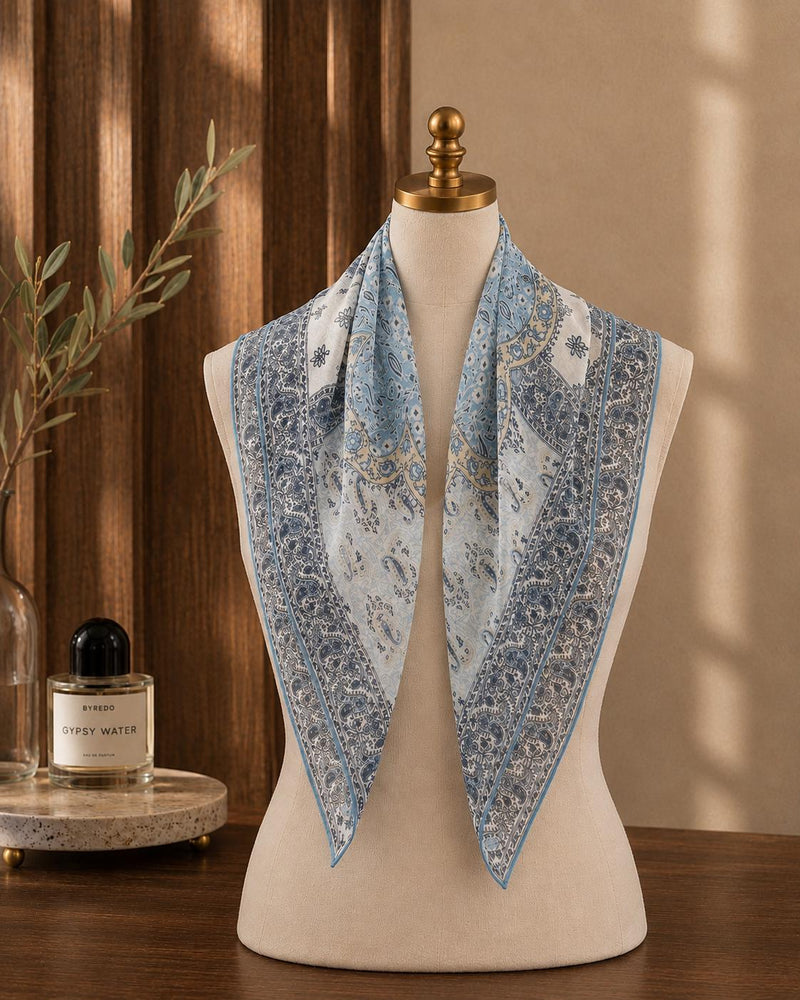 Light-blue and ivory paisley silk scarf draped on a mannequin with pointed folds.